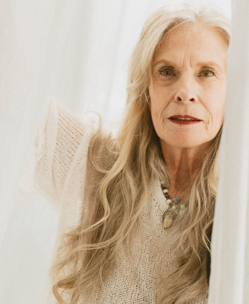 Bonnie framed by soft white curtains, gazing with quiet strength